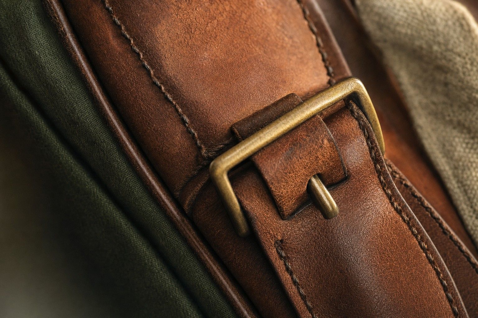 Close-up of saddle stitching on full-grain leather beside a brass buckle
